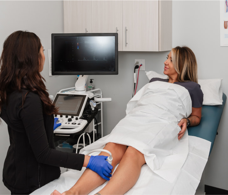 a photo of a technician performing vascular ultrasound in the lower extremeties of a patient